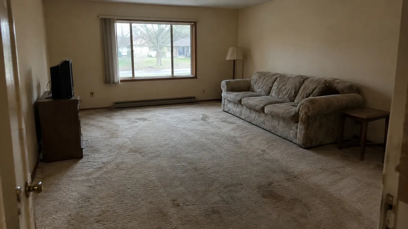 Stained Carpet Living Room Before | Music City Floor Dimly lit living room with stained beige carpet, an outdated floral sofa and a television before new flooring